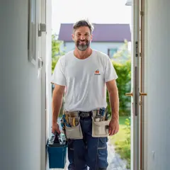 Smiling handyman in Fix Hub uniform carrying a toolbox and wearing a tool belt, arriving at a client’s home